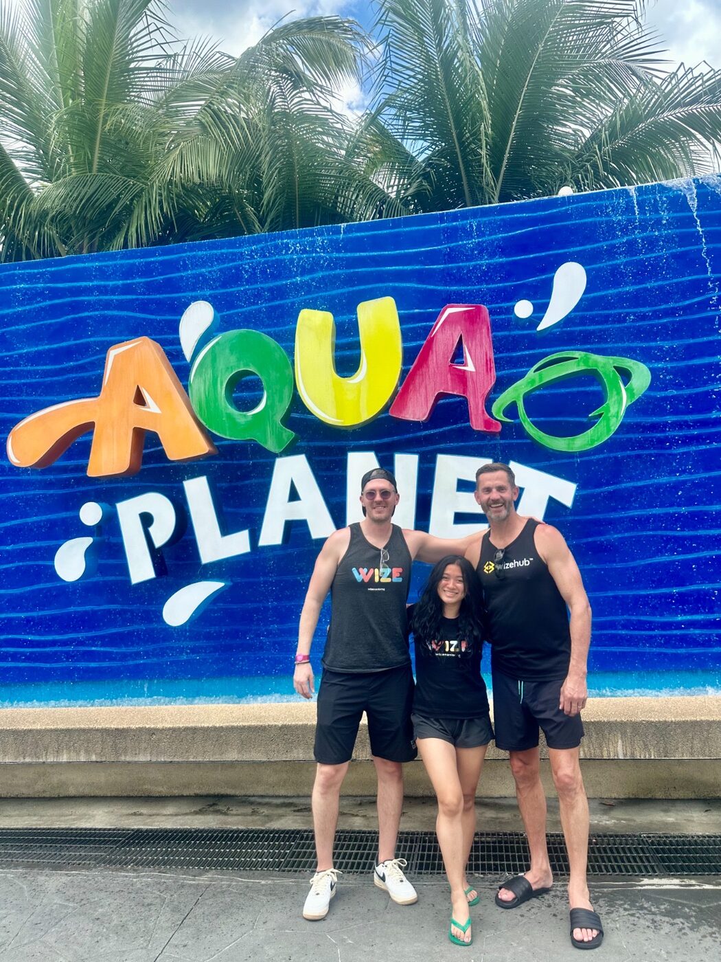 Three people with arms around each other in front of a blue water feature