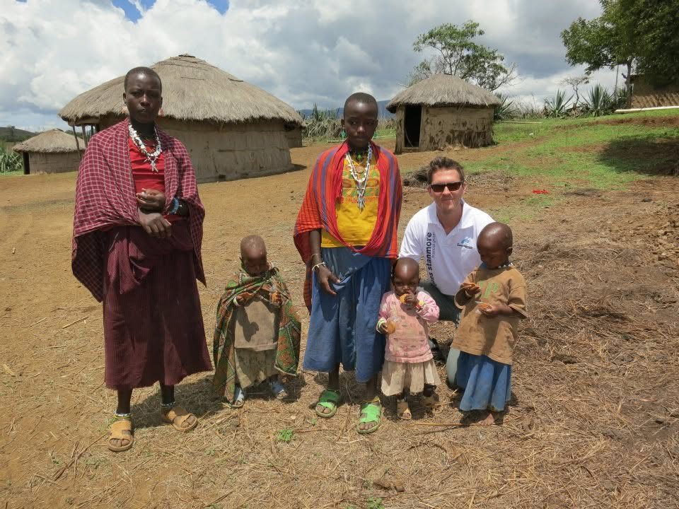 Bren with a family outside thatched huts on a trip to Africa