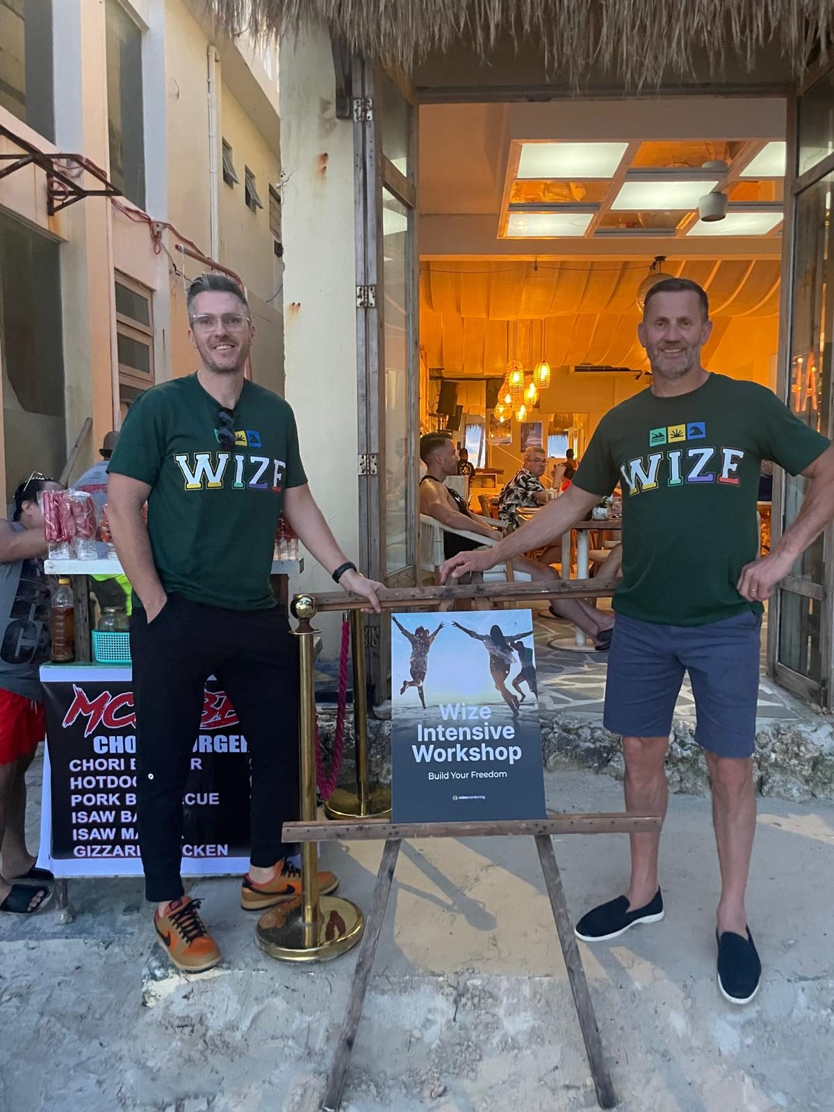 Jamie and Bren in Wize shirts beside the workshop sign