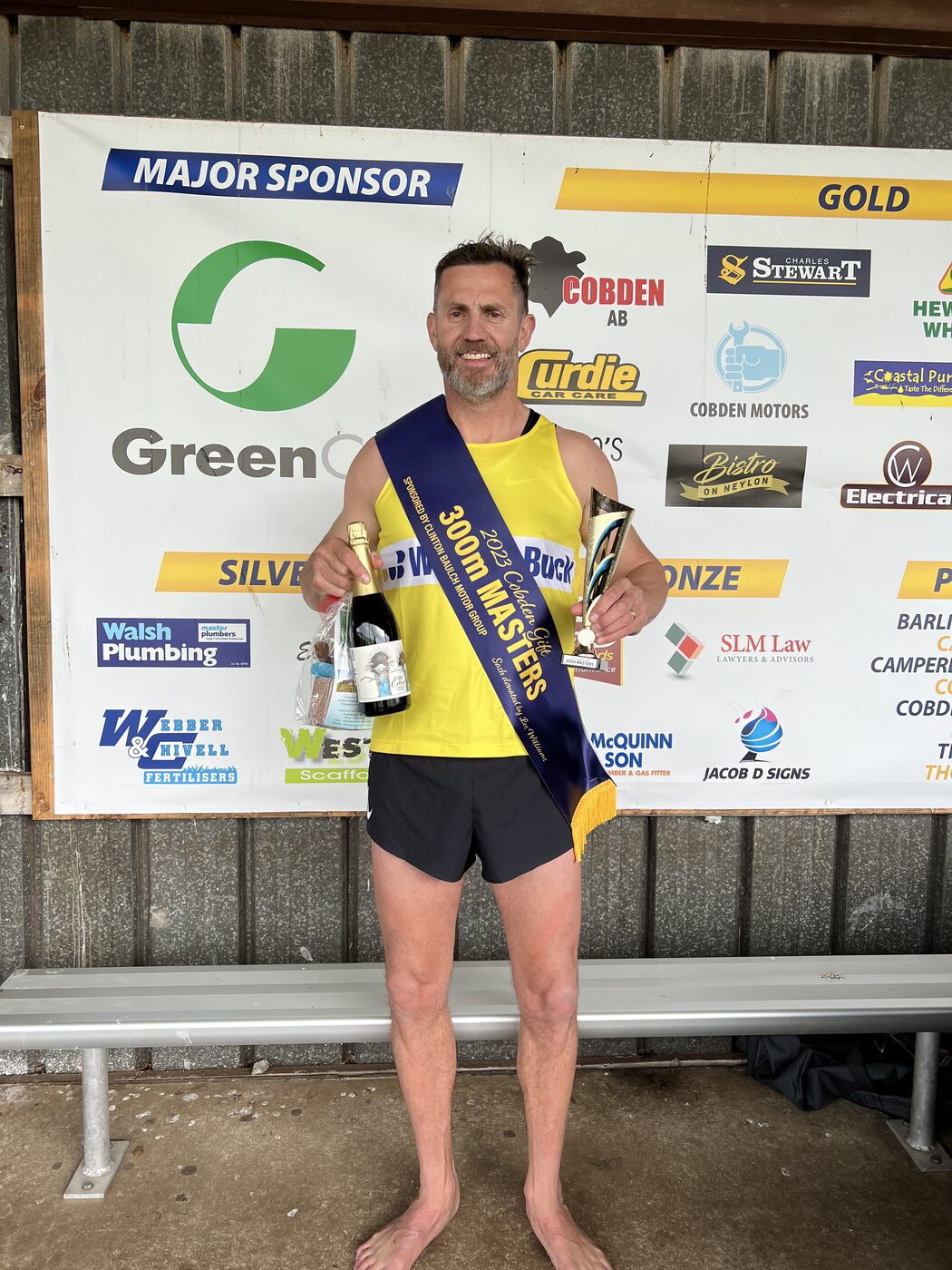 A runner in a yellow singlet holding a trophy and a bottle after a race