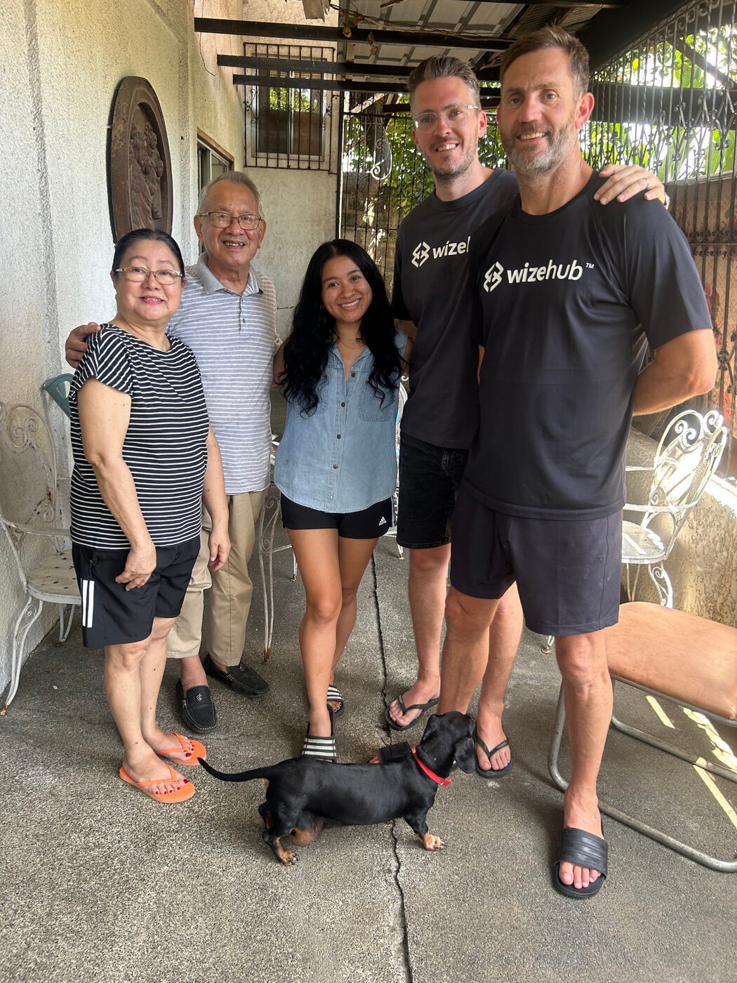 Friends and family smiling together on a patio, a dachshund at their feet