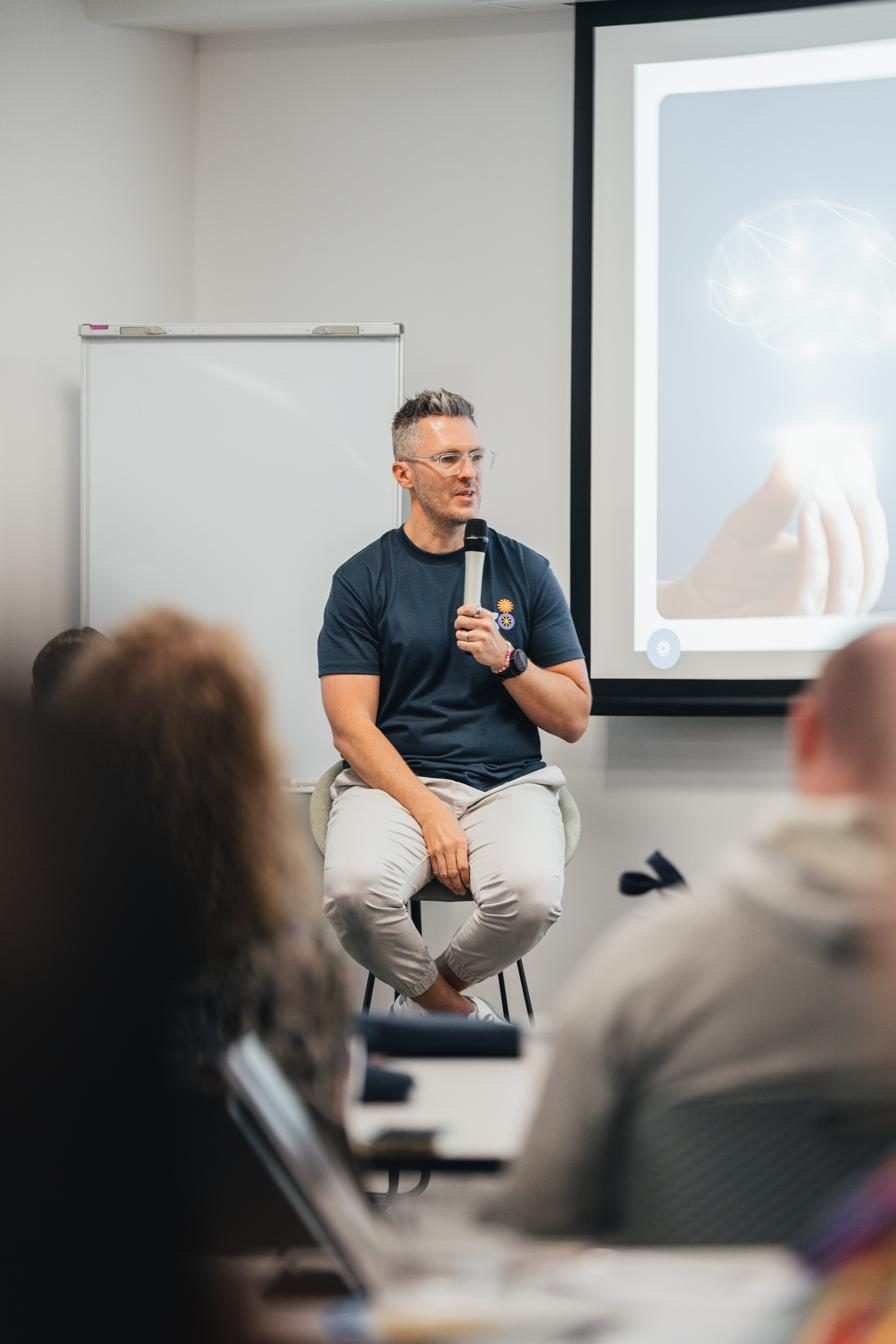 Bren answering questions from a stool in a workshop room