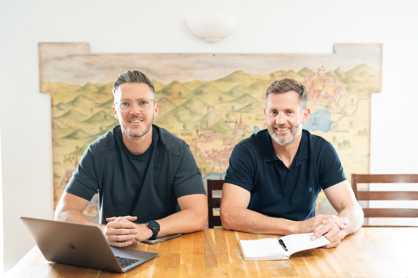 Two people at a desk with a laptop and an open notebook