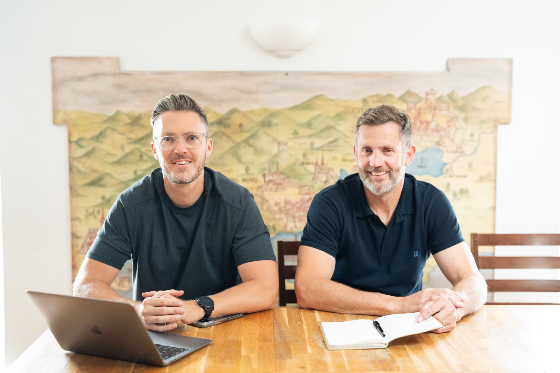 Two people working at a table with a laptop and an open notebook